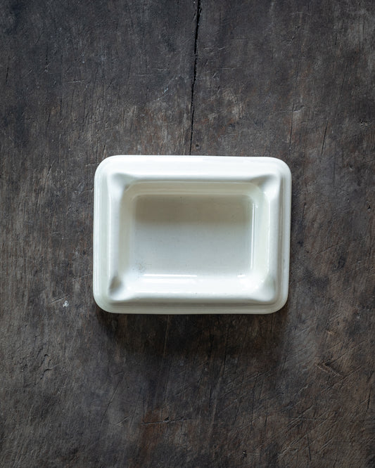 A small rectangular white ceramic dish with a raised rim, photographed from above on a dark rustic wooden surface.